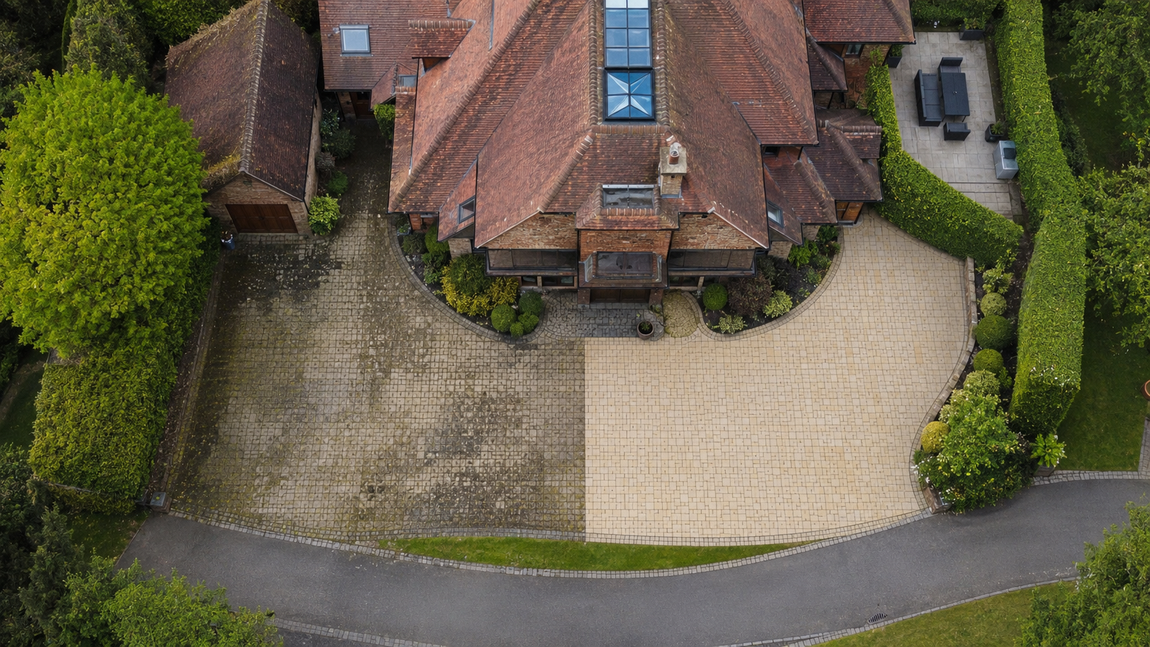 Aerial view of a large brick house with tiled roofing surrounded by mature gardens, lawn, driveway and outbuildings in a rural setting