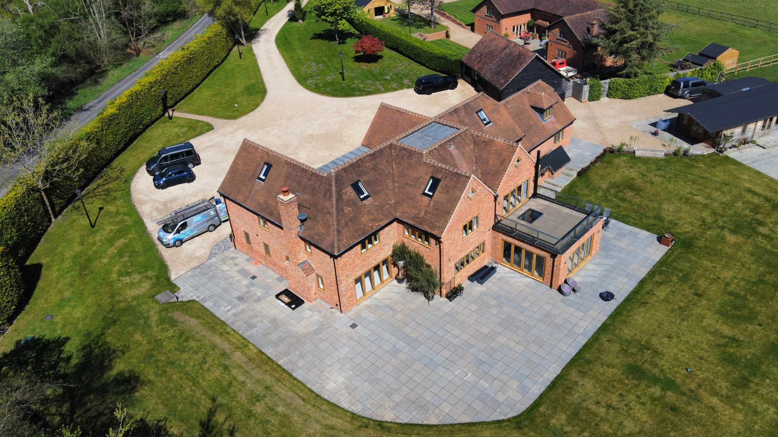 Aerial drone view of a large detached house with a clay tile roof and block paved driveway