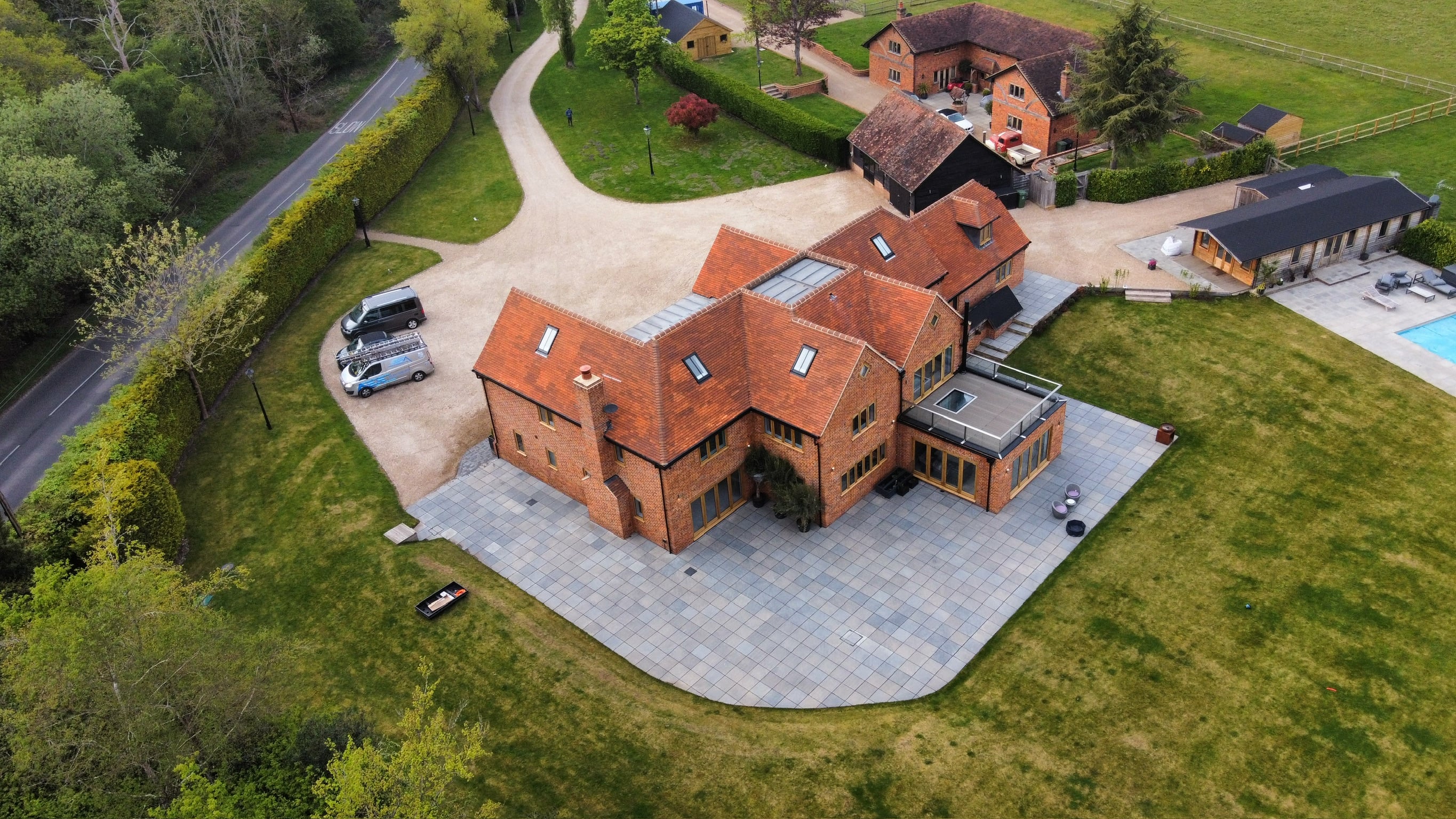 Aerial view of a substantial detached house with terracotta tiled roof, orange brick elevations, multiple gables and a block paved driveway