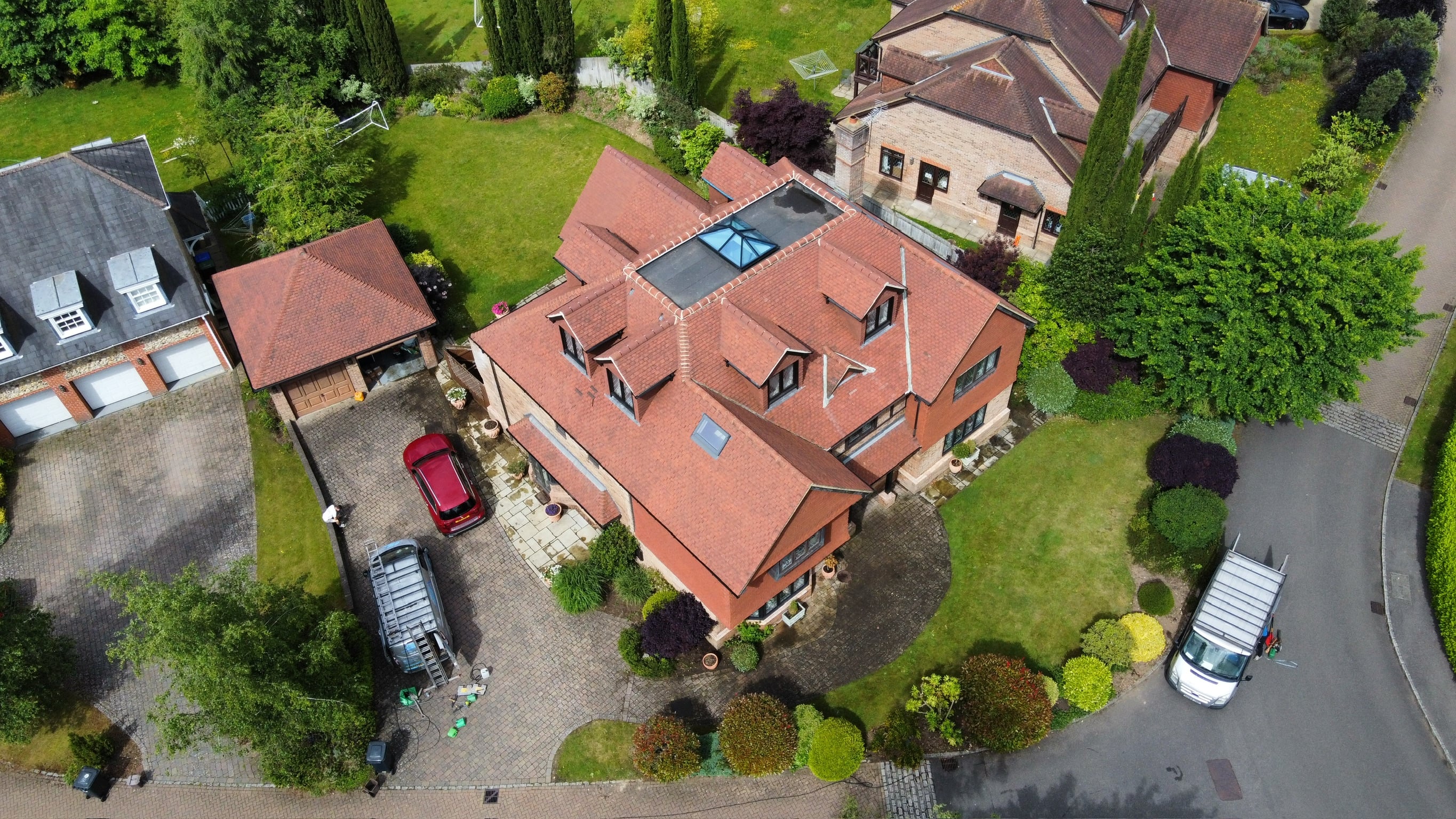 Aerial view of a large residential estate with red clay tile roofing across the main house, outbuildings and pool house, with manicured lawns and a curved driveway