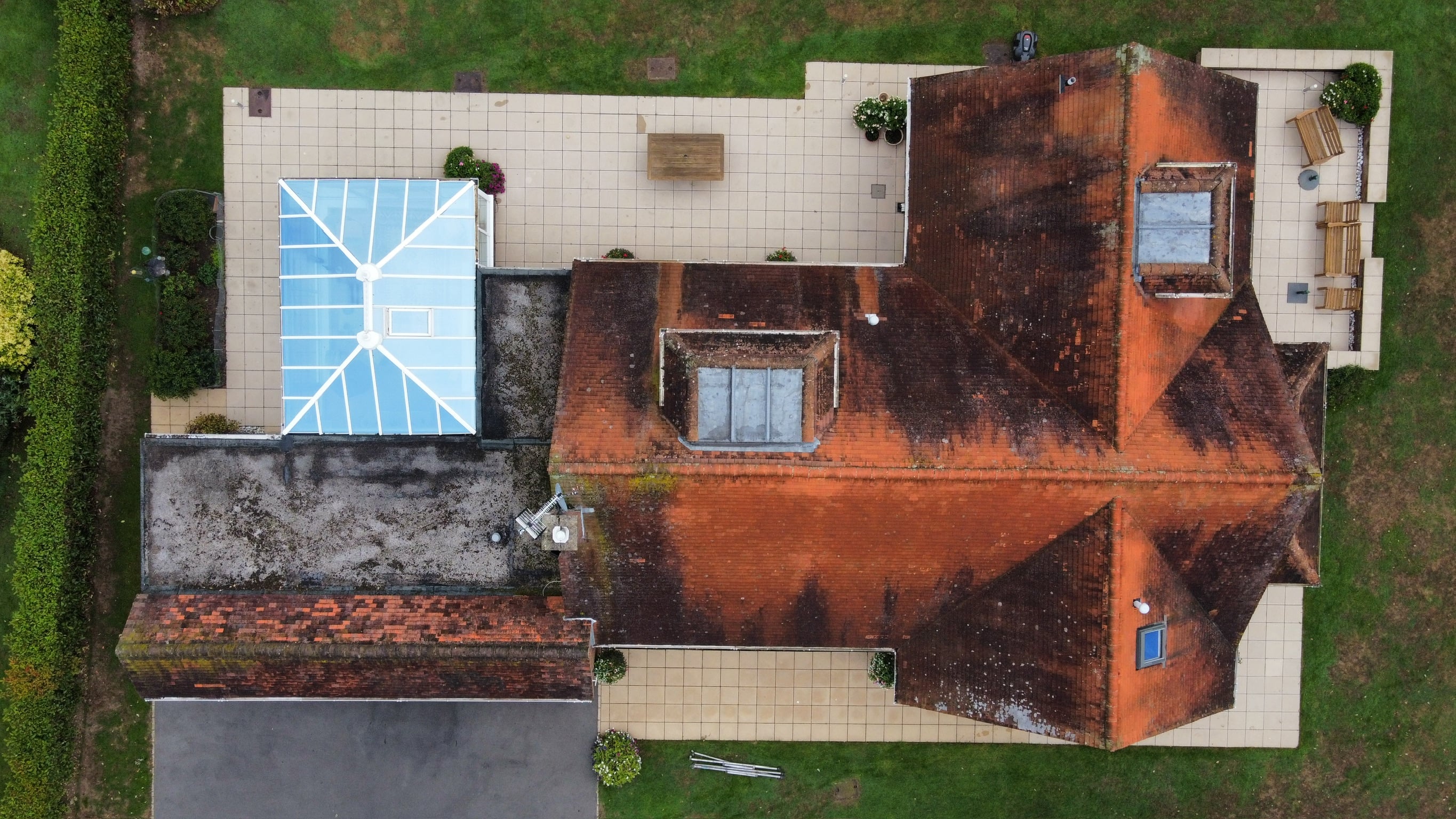 Aerial drone view of a tiled roof heavily covered in moss and lichen before cleaning